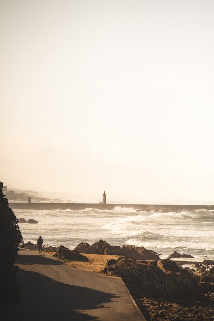 Person walks by ocean with lighthouse in distance